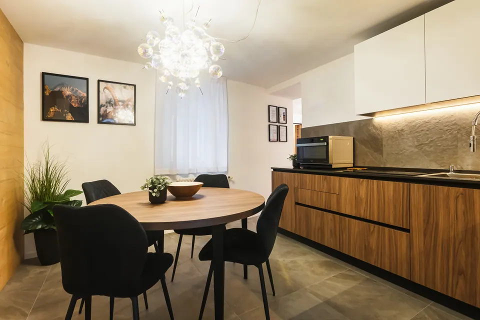 La cucina della Luna: il tavolo rotondo di legno con le sedie nere, il lampadario di bolle di vetro e i mobili di legno con il piano scuro.