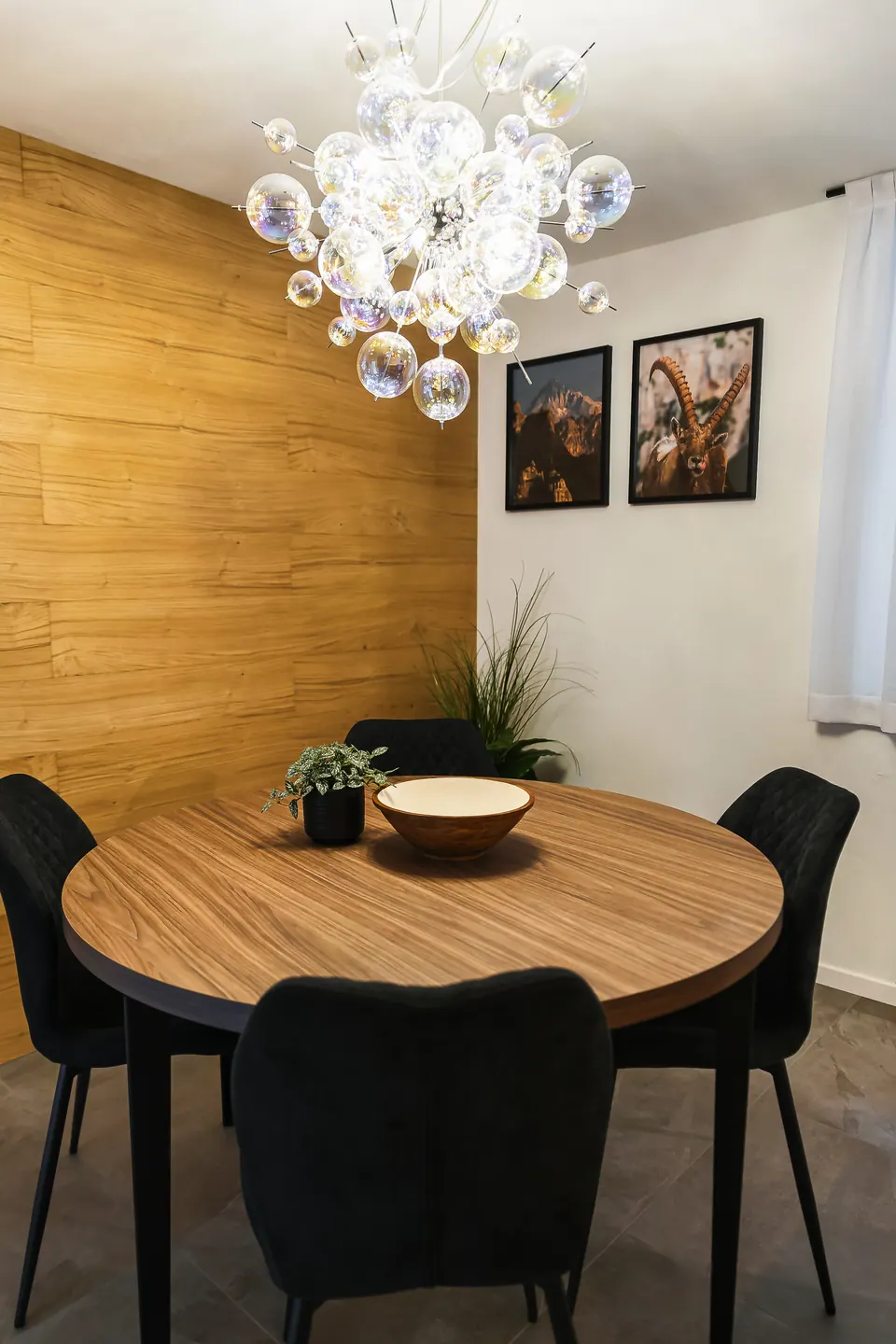 Il tavolo rotondo della Luna sotto il lampadario di vetro, davanti alla parete di rovere con due fotografie.