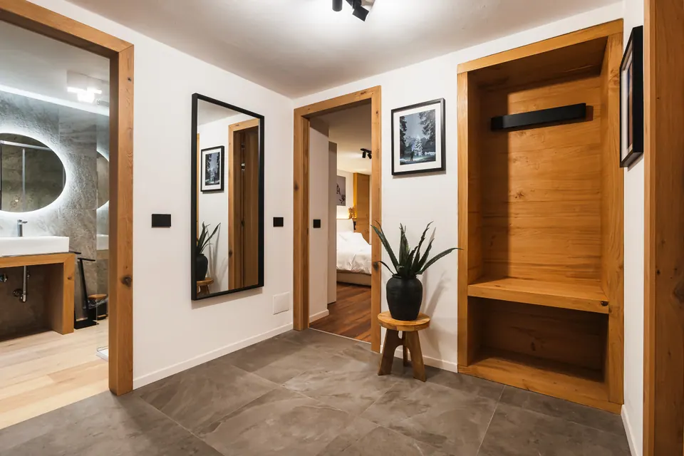 L'ingresso della Luna: lo specchio, la nicchia di legno con l'appendiabiti e la panca, una pianta e le porte del bagno e della camera.