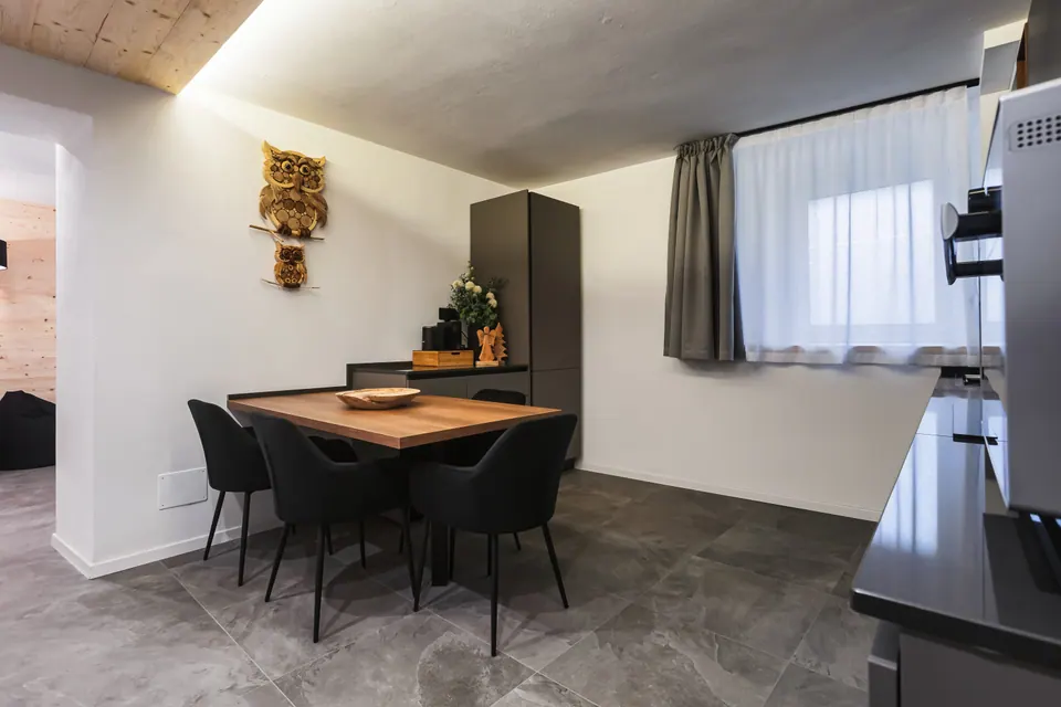 La zona pranzo del Tramonto: un tavolo di legno con quattro sedie nere, un gufo di legno appeso al muro e la finestra con le tende.