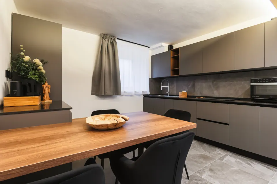 La cucina del Tramonto: un lungo tavolo di legno, i mobili antracite con il piano scuro e un vaso di fiori bianchi.
