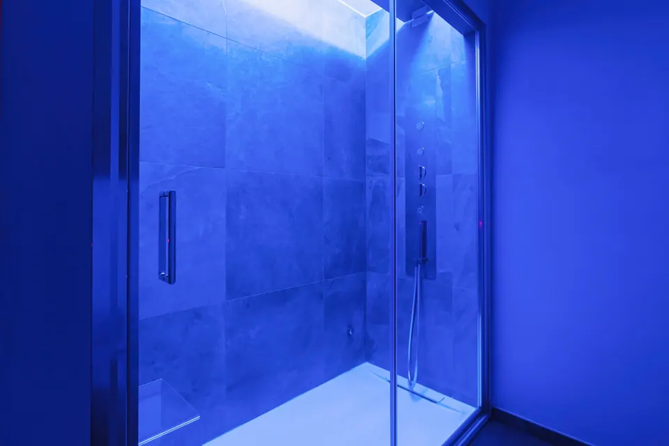 Il bagno turco del Tramonto acceso di luce blu, dietro la porta di vetro.