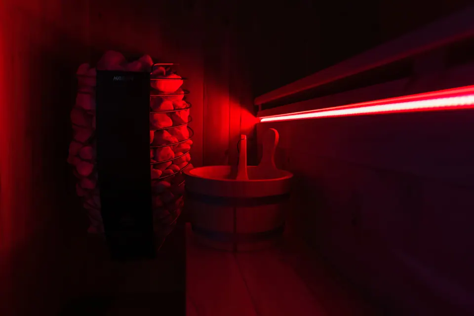 Dentro la sauna del Tramonto, nella luce rossa: le pietre della stufa e un secchio di legno.