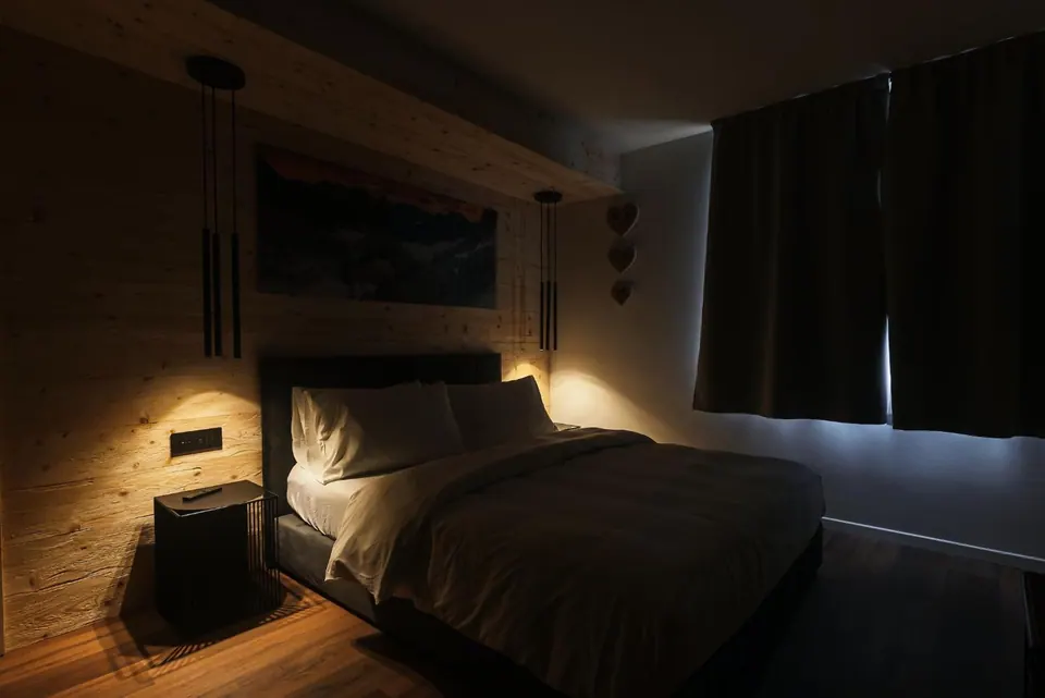 La camera del Tramonto la sera, con le luci basse: il letto, la parete di legno, le lampade a sospensione e le tende nere tirate.