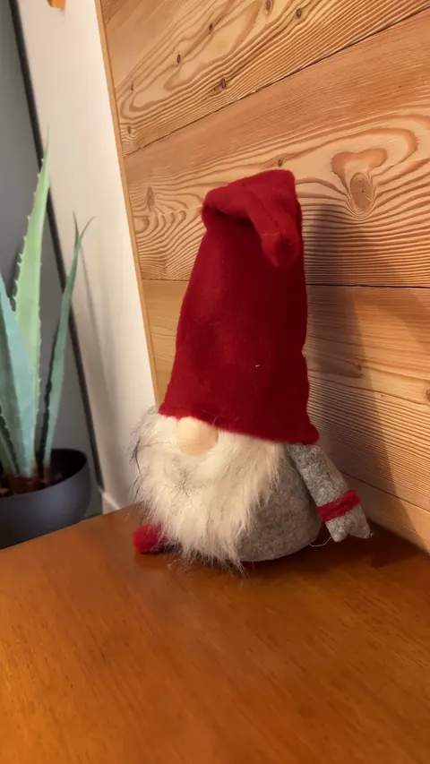 Uno gnomo col cappello rosso e la barba bianca, seduto su una cassapanca di legno intagliata contro la parete di larice della camera del Sole.
