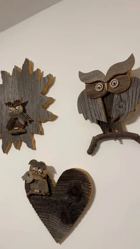 Un sole e un cuore, ciascuno con un piccolo gufo, e un gufo più grande su un ramo: tre sculture di legno sul muro bianco del corridoio del Sole.