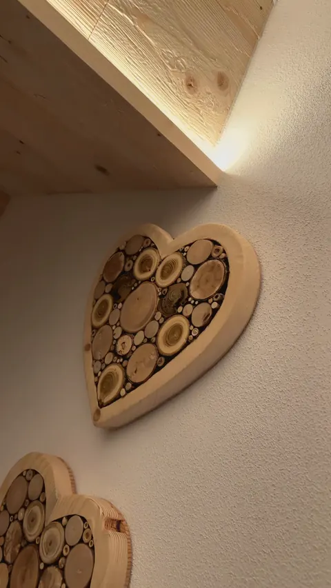 Due cuori di legno riempiti di rondelle di tronco, appesi alla parete della camera del Tramonto, nella luce calda.