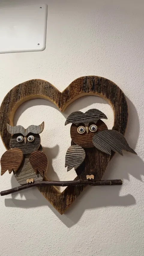 Due gufi di legno con gli occhi tondi, posati su un rametto dentro un cuore di legno con la corteccia, nel soggiorno del Tramonto.
